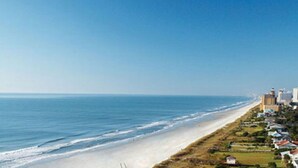 Eine Küstenansicht mit Strand, Meer und einer Reihe von Gebäuden entlang der Uferlinie.