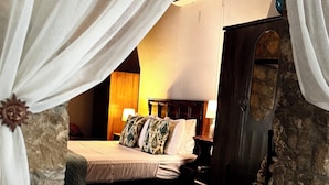 Een slaapkamer met een stenen muur, een bed met gekleurde kussens, een nachtkastje en een stoel.