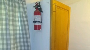 A small room with a fire extinguisher mounted on the wall, a wooden door, and a blue box on a shelf.