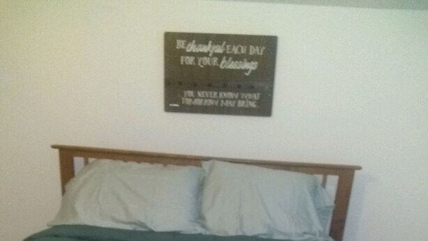 A bedroom with a bed, pillows, and a wall-mounted sign.