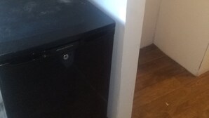 A compact black refrigerator in a corner of a room with wooden flooring and white walls.