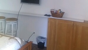 A small room with a bed, a TV mounted on the wall, a wooden cabinet, and two stools.