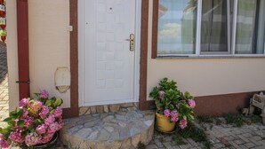 Una casa con una porta bianca, scalini in pietra e vasi con fiori rosa.