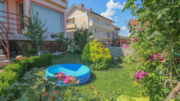 Un giardino residenziale con una piscina gonfiabile blu, diverse piante e un edificio con balconi.