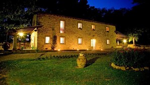 Un edificio in pietra con numerose finestre, un giardino con un vaso grande e un albero.
