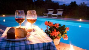 Un tavolo a bordo piscina con due bicchieri di vino, un piatto con cibo e una pianta in vaso con fiori.