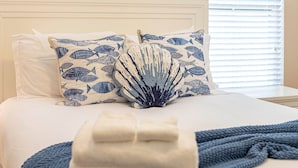 A neatly made bed with white linens, two pillows with a blue fish pattern, and a blue knitted throw.