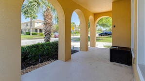 A covered outdoor area with arches, a palm tree, and a street view in the background.