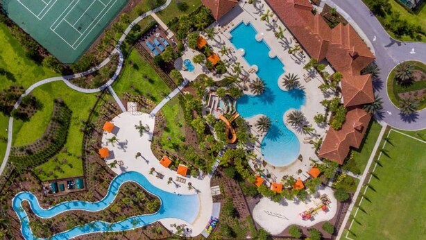 An aerial view of a resort with a large swimming pool, a tennis court, and a winding water slide.