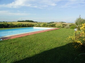 Une piscine rectangulaire bordée de rouge, entourée d’une pelouse bien entretenue et sous un ciel dégagé.