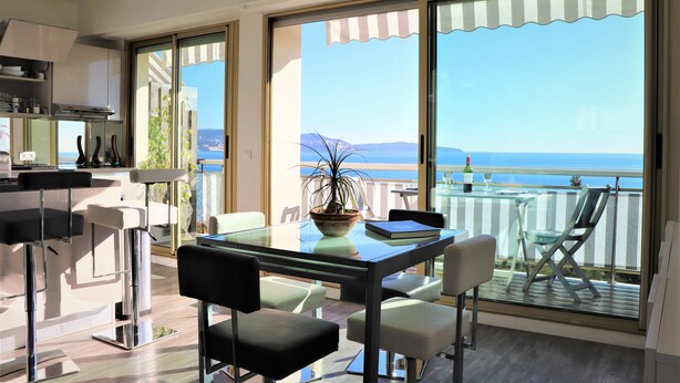 Une cuisine moderne avec une table et des chaises en verre, une plante en pot et une vue sur la mer.