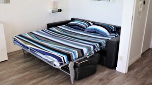 Un lit avec une couvre-lit à rayures, une table de chevet, une lampe et une étagère avec des articles de toilette.