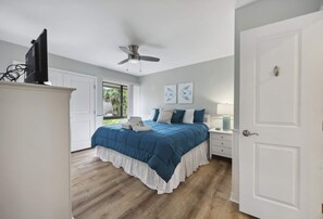 A bedroom with a bed, a ceiling fan, a white door, and a window.