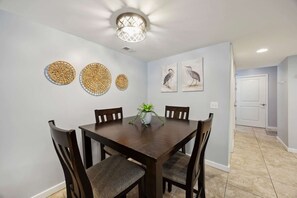 A dining area with a dark wooden table, six chairs, a potted plant, and three woven wall decorations.
