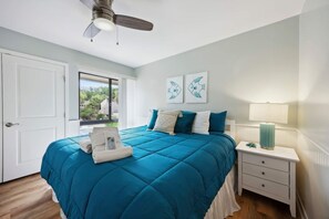 Une chambre à coucher avec un lit, une table de chevet, une lampe et des œuvres d’art accrochées au mur.