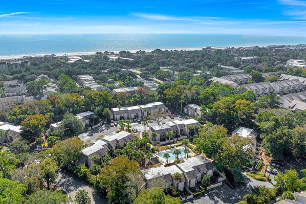 Un quartier résidentiel comprenant plusieurs immeubles, une piscine et, au loin, une plage.