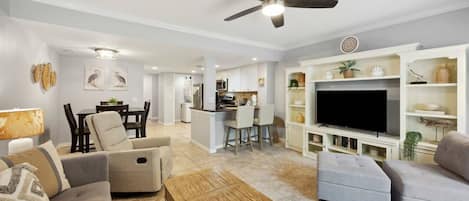 A modern living room with a flat-screen TV, sofas, a coffee table, and a ceiling fan.