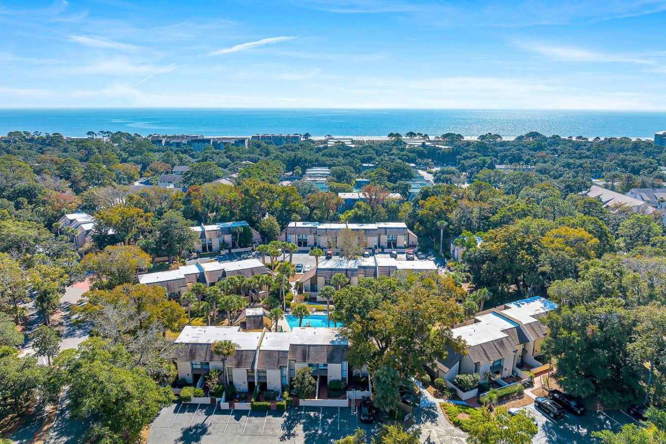 An aerial view of a residential area with multiple buildings, a swimming pool, and a view of the ocean.