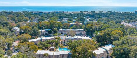 An aerial view of a residential area with multiple buildings, a swimming pool, and a view of the ocean.