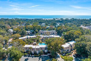 An aerial view of a residential area with multiple buildings, a swimming pool, and a view of the ocean.