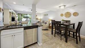 Een moderne keuken met een vaatwasser, een eetgedeelte met een tafel en stoelen, en een woonkamer met een bank en een salontafel.
