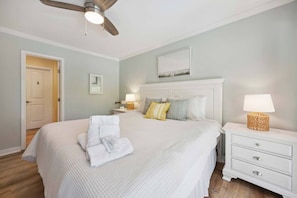 Une chambre à coucher avec un lit, des tables de chevet, un ventilateur de plafond et une porte.