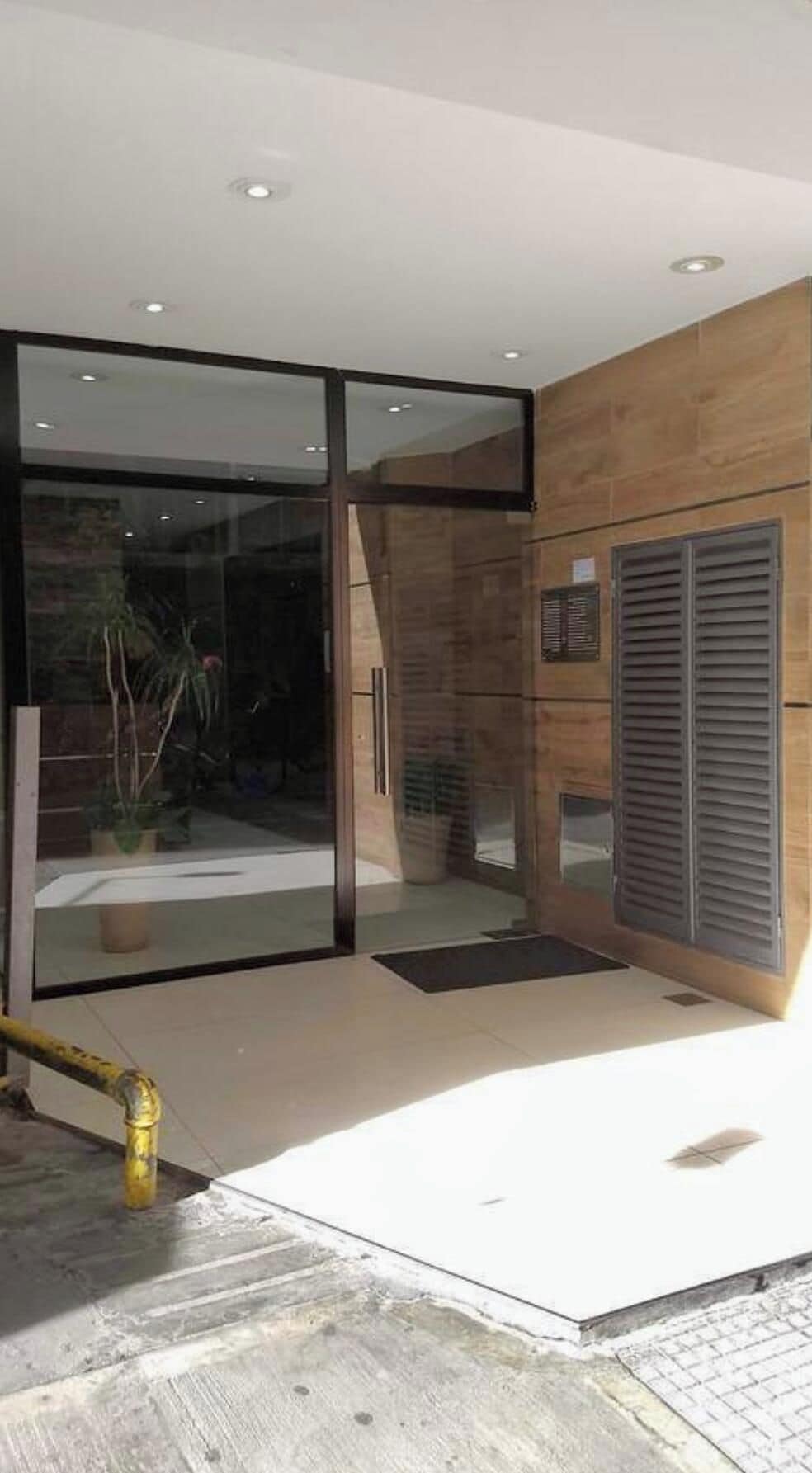 A modern interior with a glass door entrance, a wooden wall, and a metal vent.