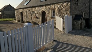 Un edificio de piedra con cerca de piquetes blancos, una entrada pequeña y un ventanal con puerta.