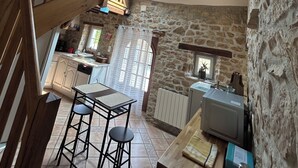 Una cocina rústica con paredes de piedra, una escalera de madera y un pequeño comedor con taburetes.