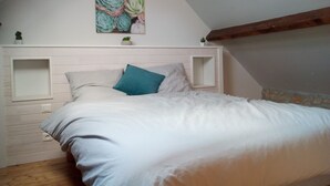 Un dormitorio con techo inclinado, una cama con ropa de cama blanca, un almohá de color turquesa y una obra de arte colgante en la pared con suculentas.