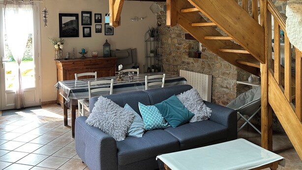 Amplia sala de estar con una escalera de madera alta, una mesa de comedor con sillas, un sofá con cojines y una pared de piedra.