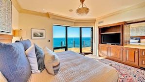 A bedroom with a large bed, a television, and a view of the ocean.