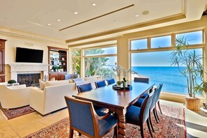 Amplia sala de estar con una gran mesa de comedor, asientos cómodos, chimenea y vista al océano.