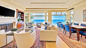 A spacious living room with a large TV, comfortable seating, a fireplace, and a view of the ocean.