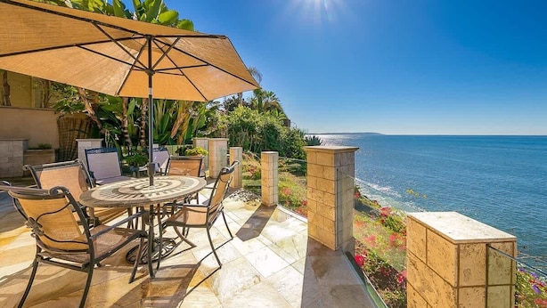 A patio with a table and chairs, a sun umbrella, and a view of the sea.
