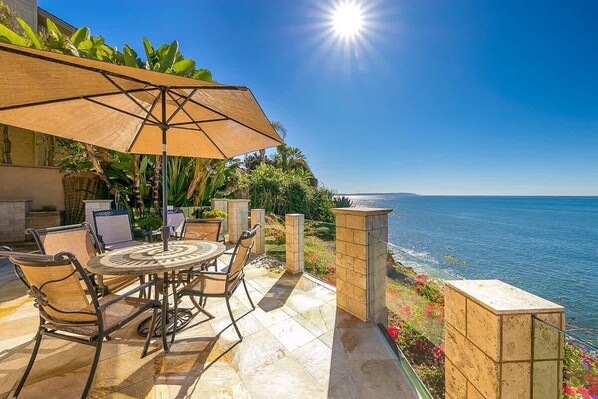 A patio with a table and chairs, a sun umbrella, and a view of the sea.