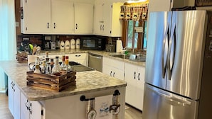 Una cocina amplia con armarios blancos, un refrigerador de acero inoxidable y una encimera de granito.