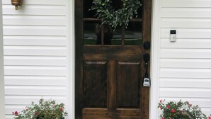 Una puerta de madera con un panel de vidrio, una lámpara colgante y dos macetas a cada lado.