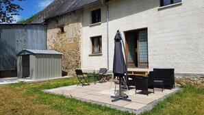 Une terrasse avec des meubles d’extérieur, un espace abrité et un bâtiment en pierre doté d’une fenêtre.