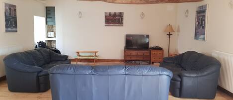 Una sala de estar con dos sofás de cuero negro, una mesa de centro de madera, un televisor sobre un mueble de madera y una lámpara de pie.