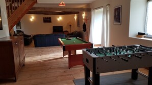 Une pièce chaleureuse équipée d’une table de billard, d’un baby-foot, d’un canapé et d’un escalier.