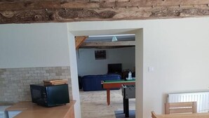 Un plancher en bois mène à un coin repas avec une table et des chaises, une petite cuisine équipée d’un four à micro-ondes, et un canapé bleu est visible au fond.