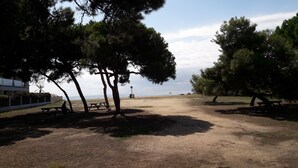 Une zone de plage avec des tables de pique-nique et des arbres, un panneau indicateur et une vue sur la mer.