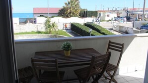 A balcony with a wooden table and chairs, a potted plant, and a view of the sea and buildings. - House 20 meters from the sea! (Fossacesia Marina)