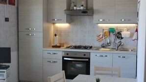 A modern kitchen with white cabinets, a gas stove, an oven, and a dining area with a table and chairs. - House 20 meters from the sea! (Fossacesia Marina)