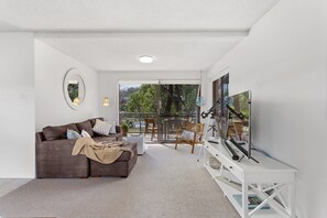 A modern living room with a brown sofa, a flat-screen TV, and a balcony with outdoor furniture.