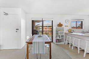 A modern kitchen with white cabinetry, a dining area with a table and chairs, and a view through a glass door.