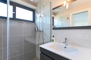 Un bagno moderno con cabina doccia in vetro, lavandino bianco con un rubinetto e uno specchio grande sopra il lavandino.