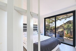 Una camera da letto con un letto, una scrivania e un'ampia porta scorrevole in vetro che dà su una zona esterna con una sedia e un tavolo.
