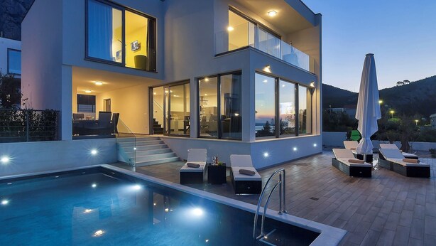 Una moderna casa a due piani con piscina, area salotto esterna e ampie finestre.